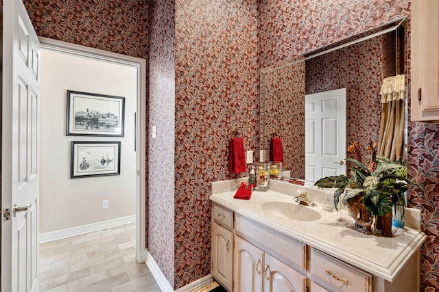 bathroom featuring baseboards, vanity, and wallpapered walls