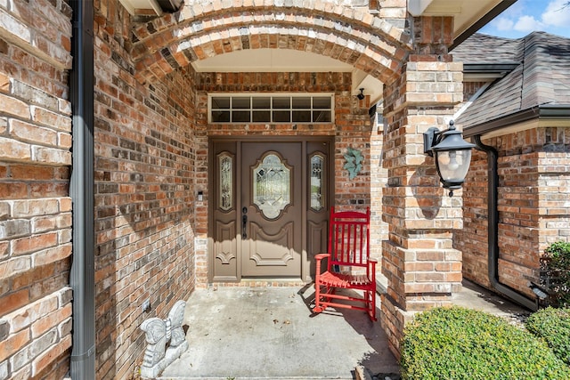 view of exterior entry with a shingled roof and brick siding