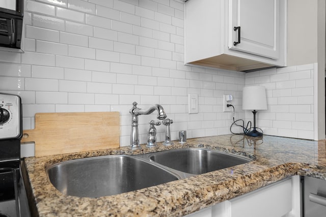 kitchen featuring tasteful backsplash, white cabinets, a sink, and light stone countertops