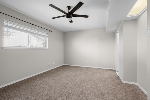 carpeted spare room featuring a skylight, baseboards, and a ceiling fan