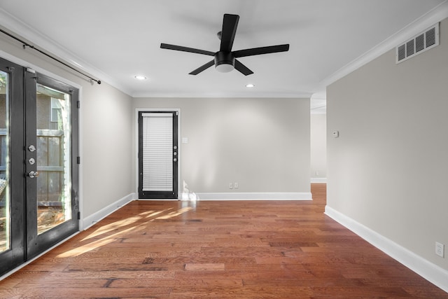 spare room with baseboards, wood finished floors, visible vents, and crown molding