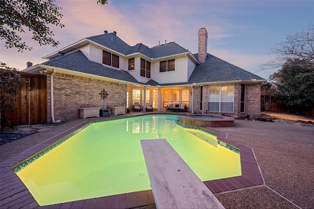 pool at dusk featuring a patio, a fenced backyard, and a pool with connected hot tub