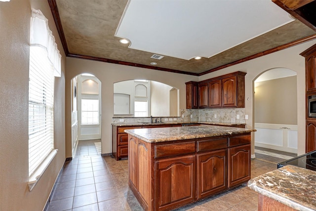 kitchen with arched walkways, decorative backsplash, a kitchen island, ornamental molding, and a sink