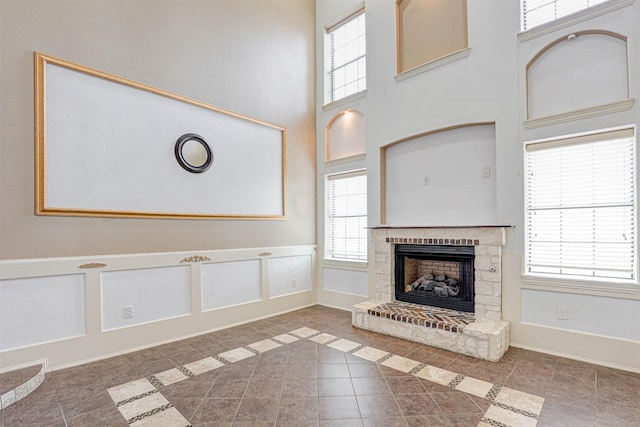 unfurnished living room featuring a fireplace with raised hearth, tile patterned flooring, a decorative wall, a towering ceiling, and baseboards