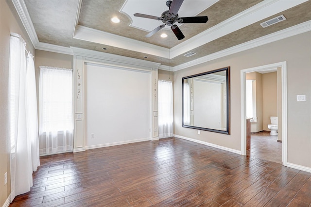 unfurnished bedroom featuring crown molding, a tray ceiling, visible vents, and dark wood finished floors