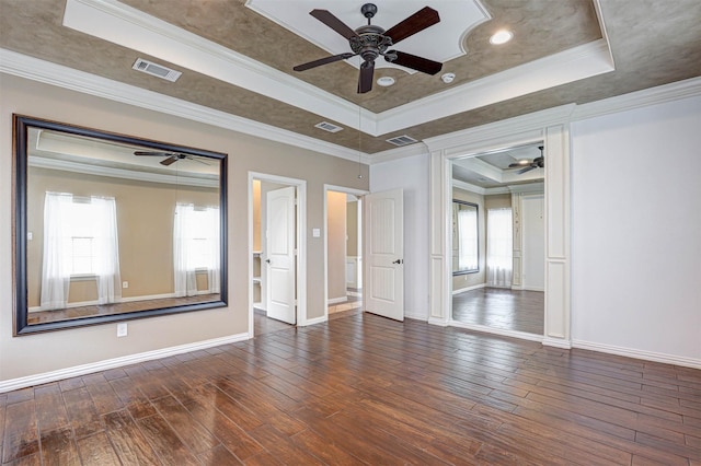 empty room with hardwood / wood-style flooring, visible vents, a tray ceiling, and crown molding