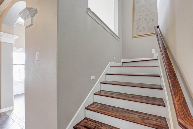 stairs with arched walkways, tile patterned flooring, decorative columns, and baseboards