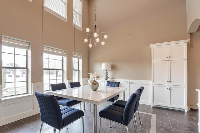 dining room featuring a decorative wall, a towering ceiling, an inviting chandelier, wainscoting, and dark tile patterned floors