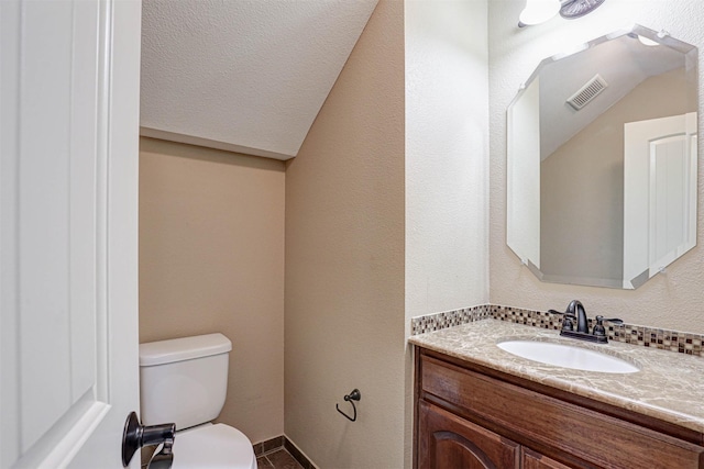 bathroom featuring visible vents, a textured wall, toilet, lofted ceiling, and vanity