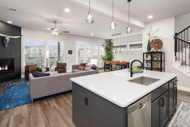 kitchen featuring a tile fireplace, dark wood-type flooring, a sink, visible vents, and stainless steel dishwasher