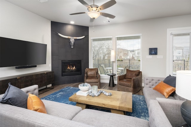 living area with ceiling fan, a fireplace, visible vents, and wood finished floors