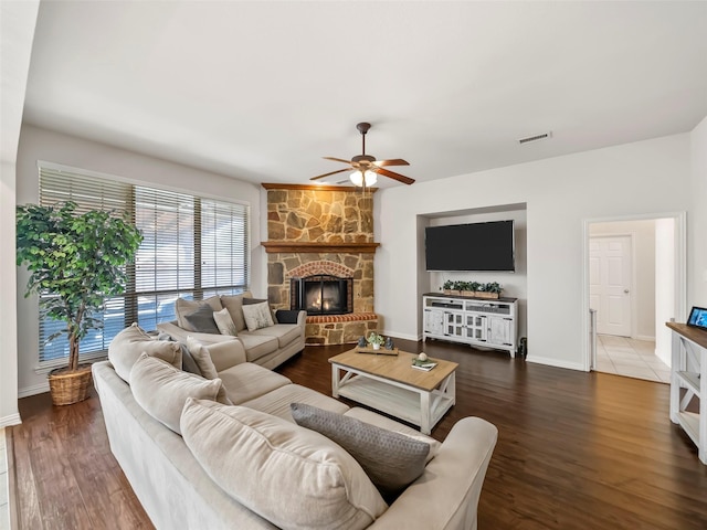 living room with a ceiling fan, visible vents, a stone fireplace, and wood finished floors