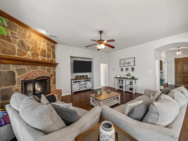 living area featuring arched walkways, visible vents, a stone fireplace, wood finished floors, and baseboards