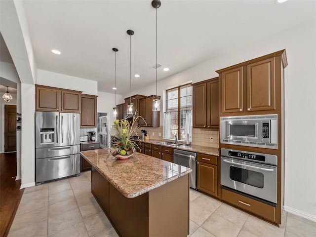 kitchen with light stone counters, a center island, decorative backsplash, appliances with stainless steel finishes, and a sink