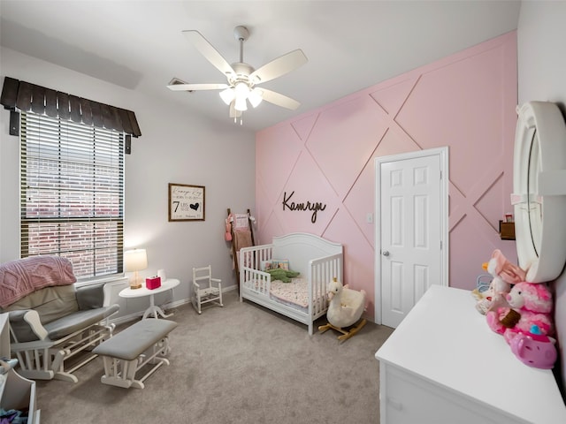 bedroom featuring a crib, baseboards, a ceiling fan, and light colored carpet