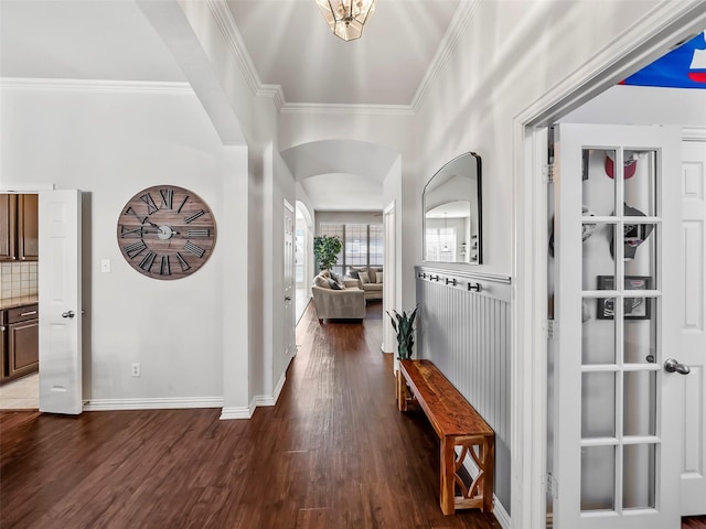 interior space featuring baseboards, crown molding, arched walkways, and wood finished floors