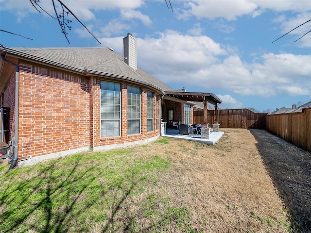 rear view of property featuring a patio, a fenced backyard, brick siding, a lawn, and a chimney