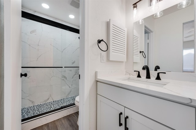 bathroom with a marble finish shower, recessed lighting, toilet, vanity, and wood finished floors