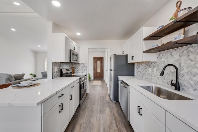 kitchen featuring light stone counters, open shelves, appliances with stainless steel finishes, white cabinetry, and a sink