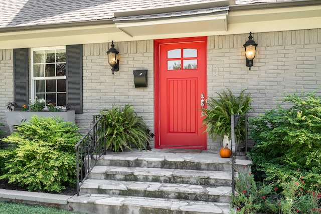 doorway to property with covered porch, a shingled roof, and brick siding