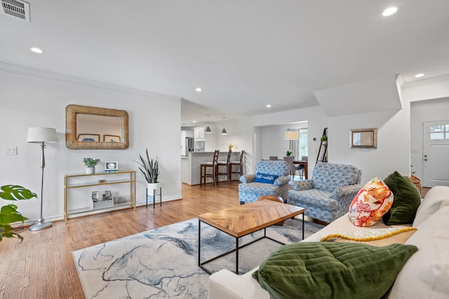 living area featuring recessed lighting, wood finished floors, visible vents, baseboards, and ornamental molding