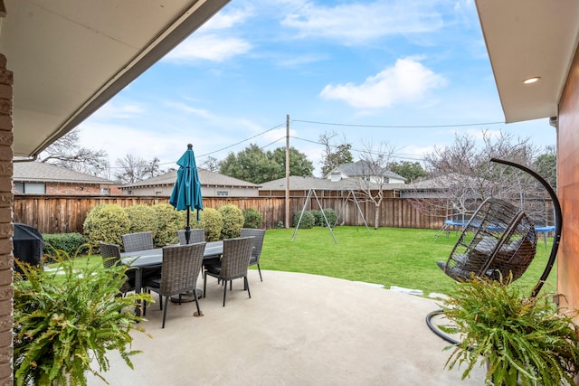 view of patio featuring outdoor dining space, a trampoline, and a fenced backyard