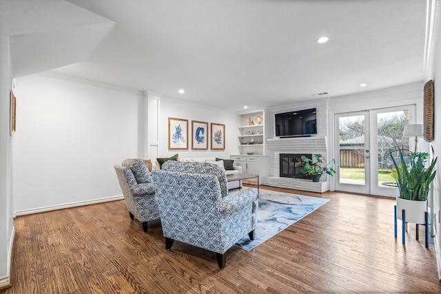 living area featuring built in features, recessed lighting, ornamental molding, a brick fireplace, and wood finished floors