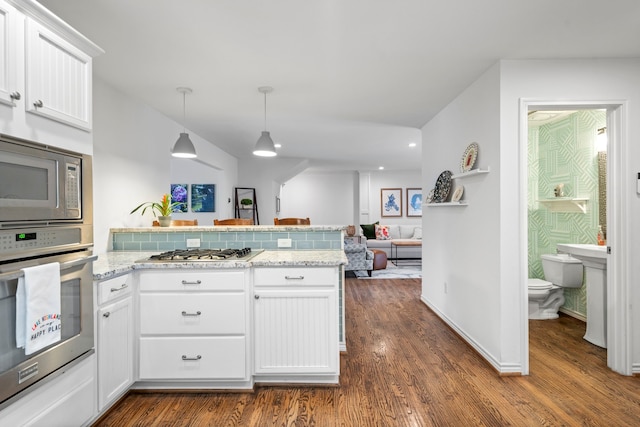 kitchen with open floor plan, dark wood-type flooring, a peninsula, stainless steel appliances, and white cabinetry