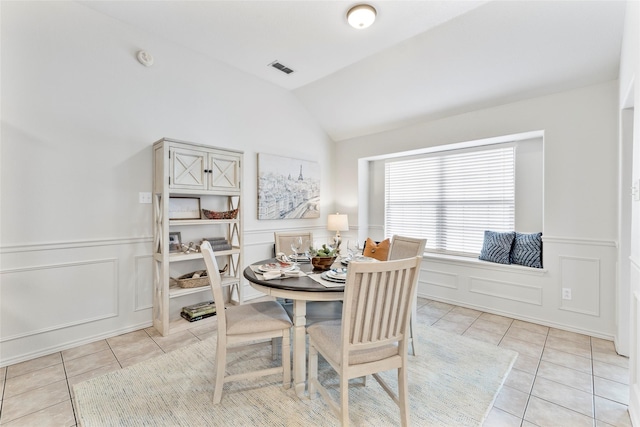 dining area featuring light tile patterned flooring, a decorative wall, a wainscoted wall, visible vents, and vaulted ceiling