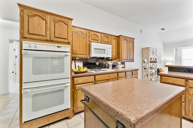 kitchen with white appliances, light tile patterned floors, a kitchen island, vaulted ceiling, and backsplash