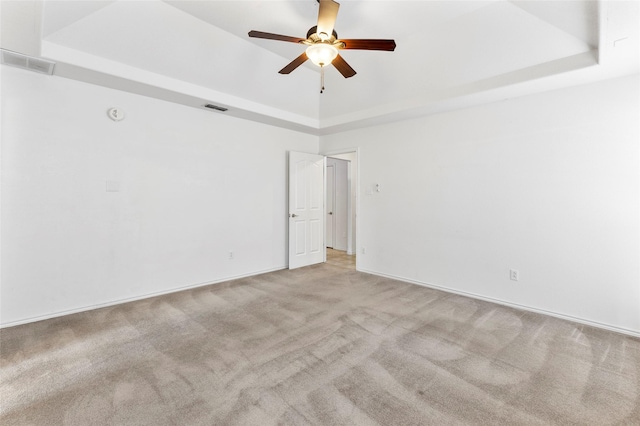 carpeted empty room featuring ceiling fan, a raised ceiling, and visible vents