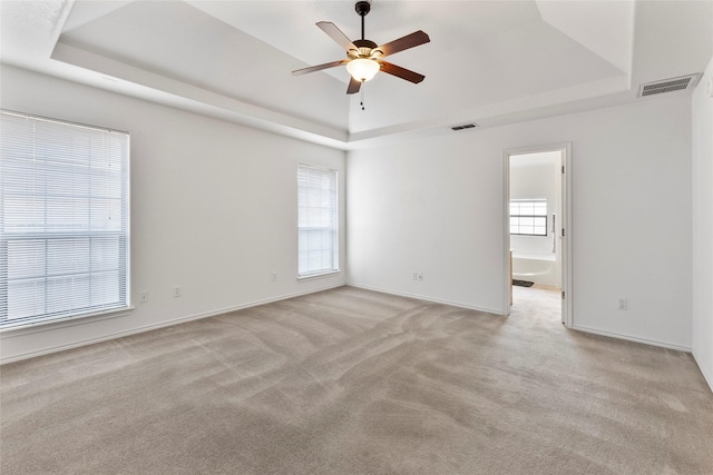 empty room featuring plenty of natural light, visible vents, and a tray ceiling