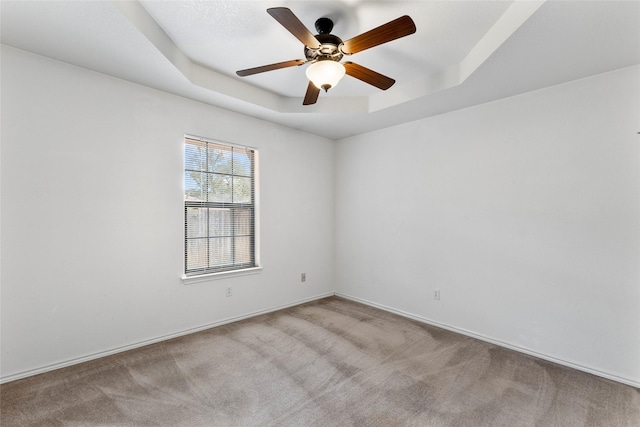 carpeted spare room featuring ceiling fan, a tray ceiling, and baseboards