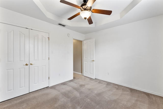 unfurnished bedroom with carpet flooring, visible vents, baseboards, a closet, and a tray ceiling