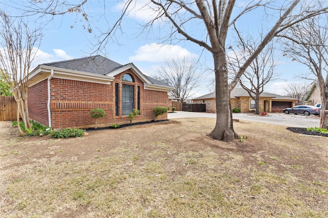 view of front of house featuring roof with shingles, fence, and brick siding