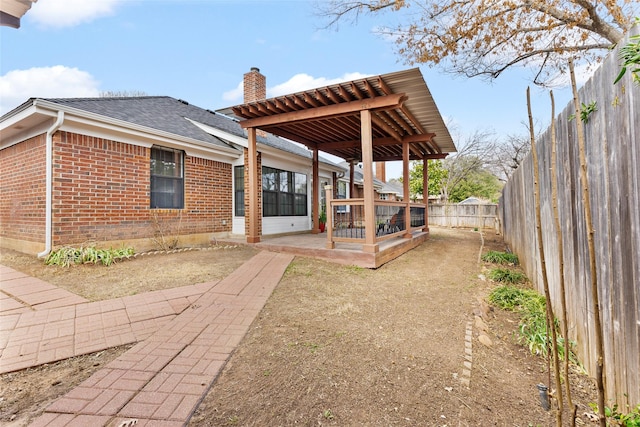 back of property with a sunroom, a fenced backyard, a chimney, roof with shingles, and brick siding