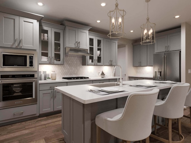 kitchen featuring a kitchen island with sink, stainless steel appliances, light countertops, gray cabinetry, and under cabinet range hood