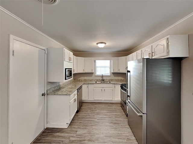 kitchen with stainless steel appliances, a sink, light wood-style floors, light stone countertops, and white cabinetry