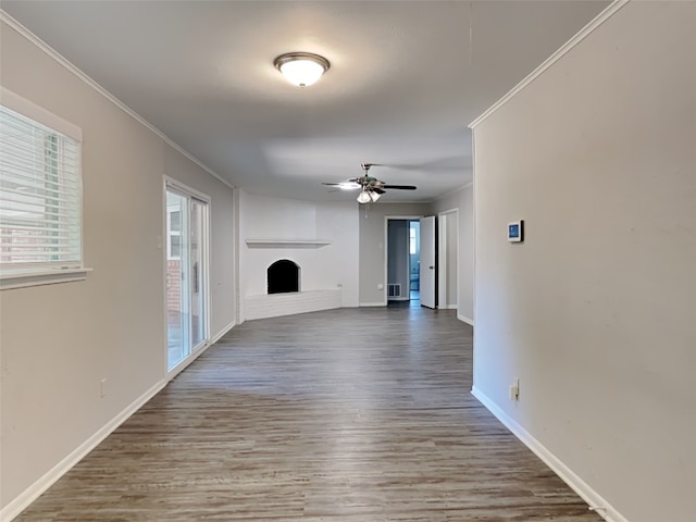 unfurnished living room featuring wood finished floors, a fireplace with raised hearth, crown molding, and baseboards