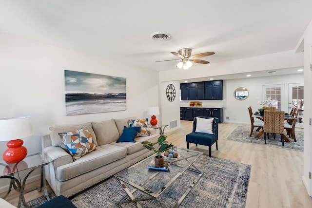 living room featuring baseboards, a ceiling fan, visible vents, and light wood-style floors