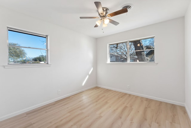 empty room with light wood-style flooring, a ceiling fan, visible vents, and baseboards