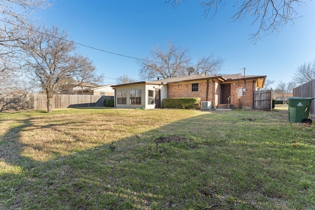 rear view of property with a sunroom, fence, a yard, central air condition unit, and brick siding