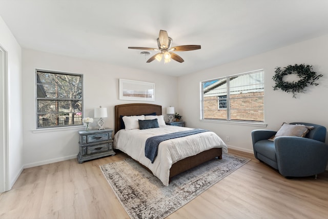 bedroom featuring a ceiling fan, multiple windows, baseboards, and wood finished floors