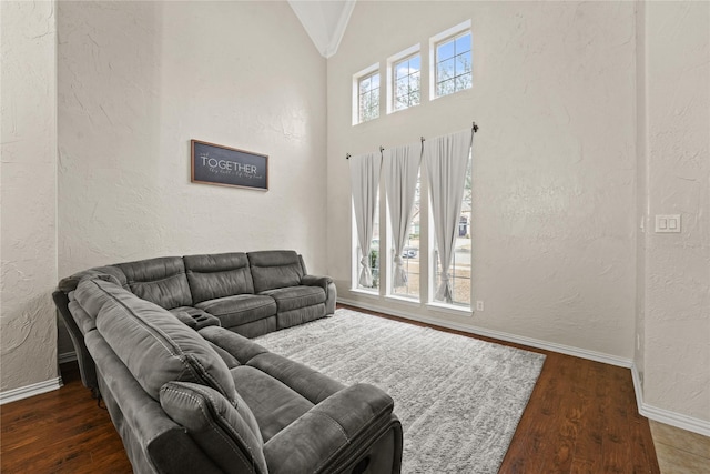 living room featuring lofted ceiling, baseboards, wood finished floors, and a textured wall