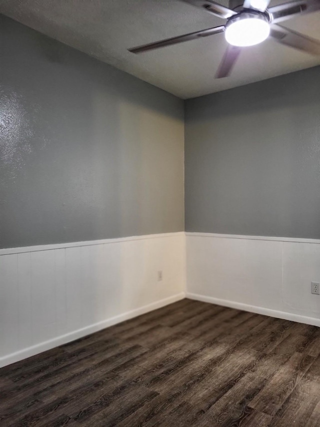 unfurnished room featuring a wainscoted wall, dark wood finished floors, and a ceiling fan