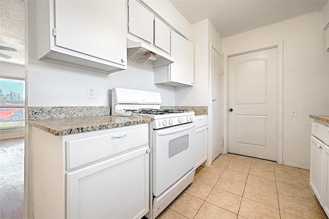 kitchen featuring a textured ceiling, light tile patterned floors, under cabinet range hood, white cabinets, and white gas range oven