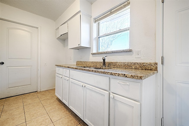 kitchen with a textured ceiling, light stone counters, light tile patterned flooring, a sink, and white cabinets