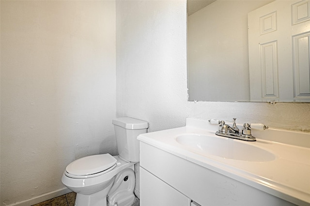 half bathroom featuring baseboards, a textured wall, vanity, and toilet