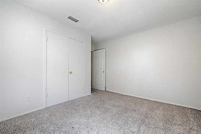 unfurnished bedroom with a closet, a textured ceiling, visible vents, and carpet flooring