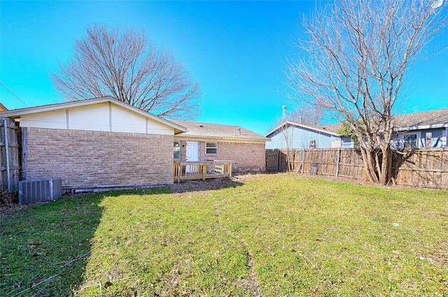 rear view of property with a yard, brick siding, a fenced backyard, and central air condition unit